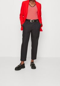 Blazer rojo sobre una camiseta sin mangas a rayas rojas y blancas, combinado con pantalones negros ajustados y mocasines negros gruesos con detalles de hardware.