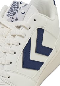 Weißer Sneaker mit marineblauen Chevron-Akzenten, Textil-Leder und Stoffzunge. Mit weißen Schnürsenkeln und perforierten Details an den Seiten.