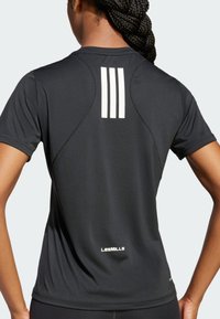 Sort sports t-shirt med rund halsudskæring, korte ærmer og tre lodrette hvide striber på ryggen. "LES MILLS" logo ved kanten.