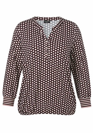 Schwarze langärmlige Bluse mit weißen Punkten, rundem Ausschnitt mit einer Knopfleiste mit drei Knöpfen und gemusterten Bündchen mit roten und weißen Streifen.