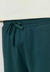 Pantalons de survêtement vert foncé avec une texture douce, une taille élastique et un cordon de serrage réglable. Design simple sans motifs ni éléments visibles.
