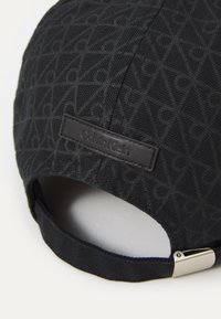 Black cap featuring a textured geometric pattern, a leather label with "Calvin Klein," and an adjustable strap with metallic hardware.