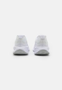 Zapatillas deportivas blancas con una parte superior de malla texturizada, collar acolchado, logo circular en el talón y una suela acolchada con patrones de agarre.