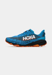 Blue athletic shoes with a textured upper, black accents, and orange Vibram outsole. Features bold "HOKA" logo and black speckled design.
