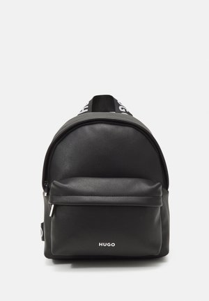 Sac à dos en cuir noir avec poche zippée à l’avant et logo Hugo, avec des bretelles noires et blanches griffées, présenté sur fond blanc.