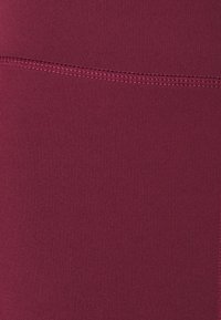 Leggings burdeos hechos de material elástico, con una textura suave y una costura plana en la cintura, que proporcionan un aspecto sin costuras.