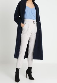 Marinblå lång stickad kappa, ljusblå linneöverdel, vita skräddarsydda byxor med bälte och rund spänne, samt svarta klackade ankelstövlar.