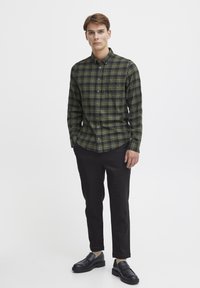 Grønn og svart rutete skjorte med knapp, med krage og lange ermer, kombinert med svarte smale bukser og svarte loafers.