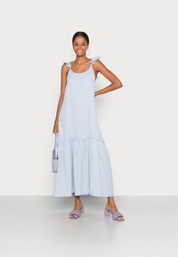 Šviesiai mėlyna maksi suknelė su raukinėtais petnešomis, kelių lygių dizainu ir tekstūruotu audiniu. Derinama su levandų spalvos platforminiu batų modeliu ir mažomis rankinėmis.