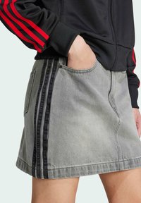 Falda de mezclilla gris con acentos de bandas negras laterales, que presenta un corte clásico, bolsillo frontal y detalles de costura visibles.