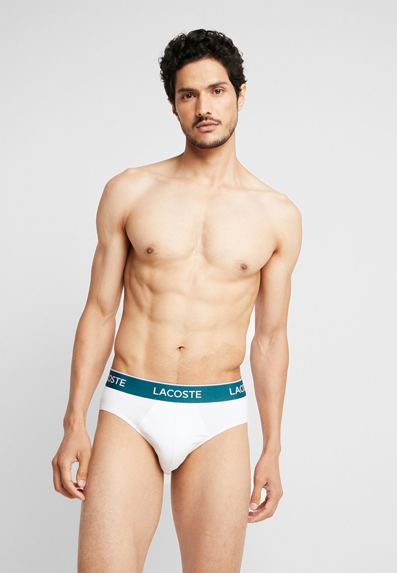 Bóxer de algodón blanco con una banda elástica en tono verde oscuro con el logo de Lacoste; diseño ajustado con una textura suave y un detalle mínimo.