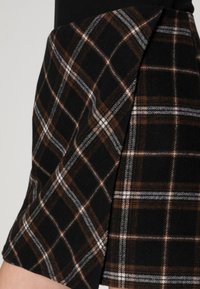 Černá a hnědá károvaná sukně s texturou připomínající vlnu, rovný lem a detail s bočními záhyby, s bílými a šedými akcenty v vzoru.