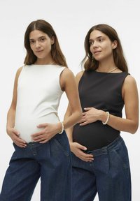 Deux mannequins enceintes portent des hauts ajustés sans manches — l'un blanc, l'autre noir — associés à des jeans en denim amples, mettant en valeur des textures lisses et des designs simples.