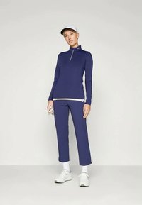 Tumes sinine spordiriietus, millel on pikaaeriline topp, millel on pooltõmbe ja sobivad lühikesed püksid. Valge müts ja kingad lõpetavad välimuse.