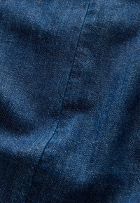 Gros plan sur un tissu denim bleu montrant une texture détaillée et une couture verticale au centre.