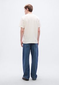 Κρεμ βαμβακερό t-shirt με κοντά μανίκια, σε συνδυασμό με μπλε τζιν παντελόνι φαρδιάς γραμμής που διαθέτει δύο πίσω τσέπες και άνετη εφαρμογή.