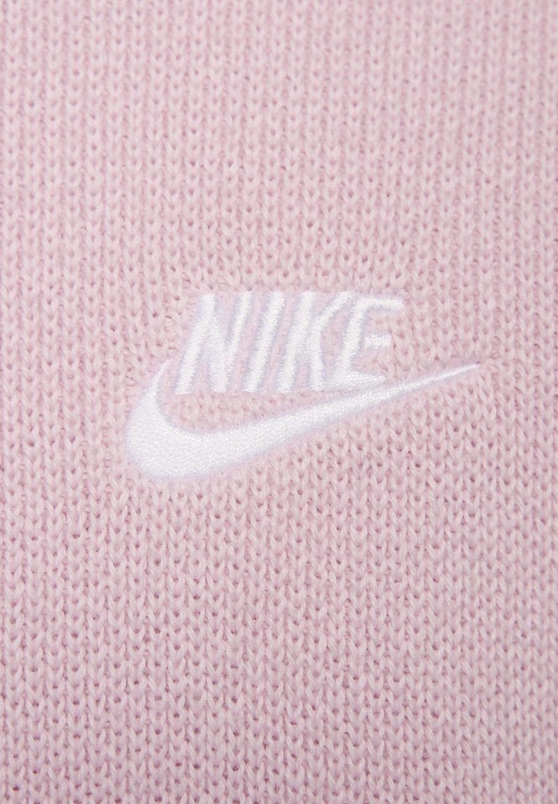 Jasnoróżowa dziana tkanina z haftowanym białym logo Nike. Tekstura jest miękka, o gładkim wykończeniu i regularnym wzorze ściegów.