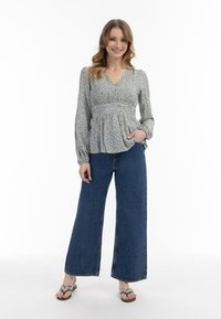 Virágmintás blúz, illeszkedő felsőrésszel és peplum derékkal, széles szárú kék farmernadrággal párosítva. A modellen lapos szandál van.