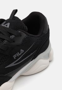 Schwarzer Sport Schuh aus einer Kombination von Wildleder und Mesh-Materialien, hervorgehoben durch ein graues Logo und subtile strukturierte Akzente auf der Sohle.