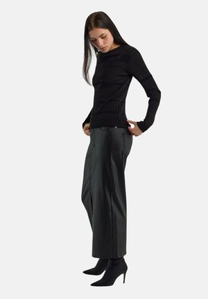 Maglione nero a coste con maniche lunghe abbinato a pantaloni neri in ecopelle a vita alta e gamba dritta, e stivali neri con tacco e punta affilata.