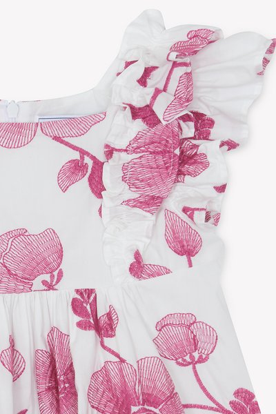 Λευκό φόρεμα από ύφασμα με ροζ κεντήματα λουλουδιών, διαθέτει λουράκια με βολάν και ζώνη στη μέση με πιέτες. Η υφή προσθέτει λεπτομέρεια στο σχέδιο.
