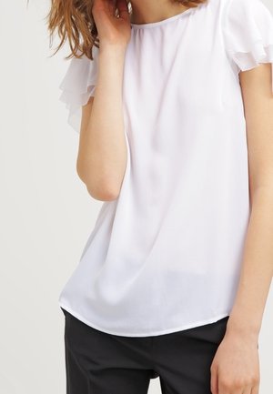 Blusa bianca con maniche trasparenti a volant, scollatura rotonda e un tessuto morbido e leggero. Orlo leggermente curvato nella parte inferiore.