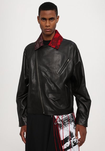 Black leather jacket with a contrasting red patterned collar, asymmetric zip front, and zippered pockets. Chunky, textured fabric accents.