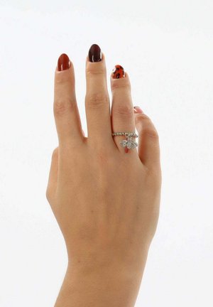 Anello d'argento con piccolo disegno di farfalla, caratterizzato da un accento rosso. Indossato su una mano con smalto per unghie dai colori misti, inclusi motivi scuri e maculati.