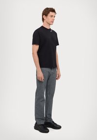 T-shirt in cotone nero, collo rotondo, design semplice; abbinato a jeans grigi e sneakers nere con dettagli dorati. Outfit semplice e casual.