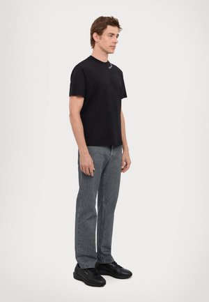 T-shirt in cotone nero, collo rotondo, design semplice; abbinato a jeans grigi e sneakers nere con dettagli dorati. Outfit semplice e casual.