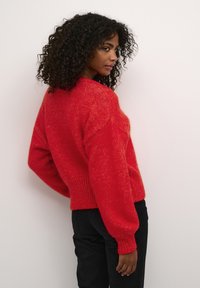 Maglione rosso lavorato a maglia con una vestibilità ampia, lunghezza cropped e finitura testurizzata. Polsini e orlo a coste, abbinato a pantaloni neri.