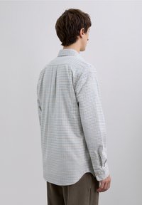 Koszula na guziki w jasnoniebiesko-biały wzór w kratę, z długimi rękawami, klasycznym kołnierzykiem i zaokrąglonym dołem. Wykonana z bawełny.