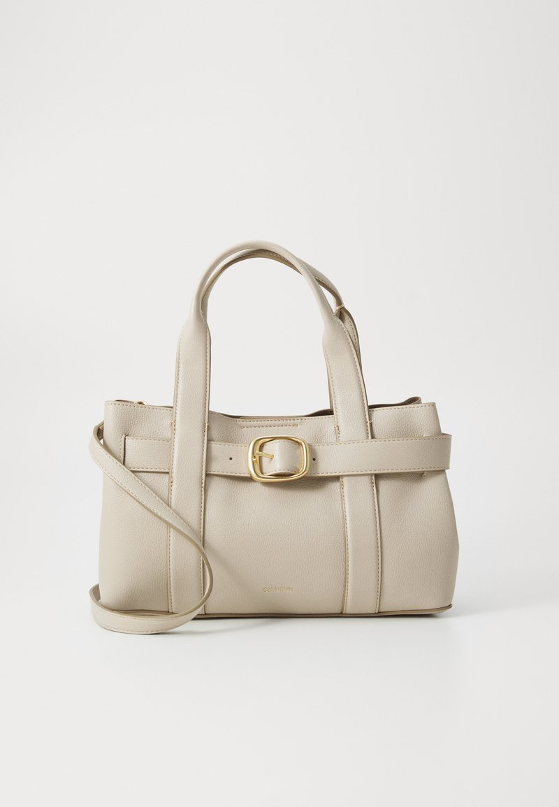 Sac à main beige en cuir texturé, avec un design structuré, des poignées supérieures, une bandoulière détachable et un accent en boucle dorée.