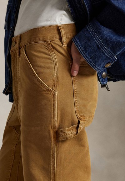 Svetlo rjave, teksturirane hlače z diagonalnimi sprednjimi žepi in stranskim žepom za tovor. Kombinirane z denim jakno v kontrastni modri barvi.