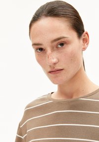 Braun gestreiftes T-Shirt mit horizontalen weißen Streifen, Rundhalsausschnitt und weicher Textur, getragen von einer Person mit neutralem Ausdruck.