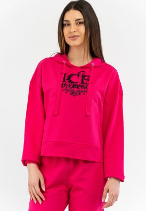Fuchsia hoodie with a black graphic print, front pocket, and drawstrings. Smooth texture and loose, cropped design. Paired with matching bottoms.