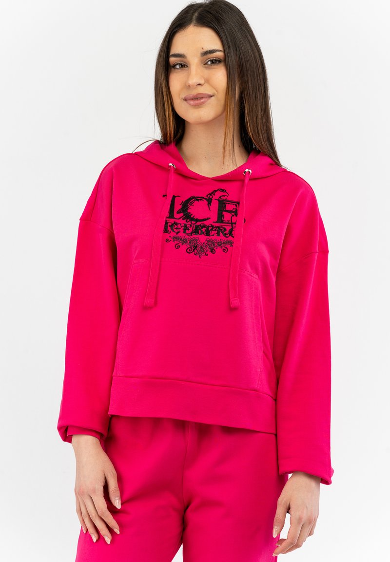 Felpa fucsia con stampa grafica nera, tasca frontale e cordini. Tessuto morbido e design largo e corto. Abbinata a pantaloni coordinati.