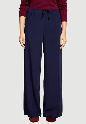 Femme portant un pantalon large bleu marine ample avec une taille à cordon et un haut bordeaux à manches longues, debout les bras détendus le long du corps.