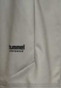 Jasnoszara tkanina sportowa o gładkiej fakturze. Zawiera czarne logo "hummel" oraz tekst "SPORTSWEAR" w lewym dolnym rogu.