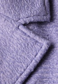 Tessuto di lavanda a trama con un aspetto morbido e peloso, caratterizzato da un motivo ondulato e bordi puliti, creando un effetto a strati.