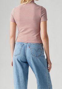 Raitapaitainen lyhythihainen toppi punaisena ja valkoisena, yhdistettynä vaaleansinisiin farkkuihin, joissa on klassinen viiden-taskun muotoilu ja kaareva ommel.