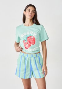 Camiseta de algodón en verde menta con un gráfico de fresas rojas y el texto "BERRY SPECIAL". Combinada con pantalones cortos elásticos de cintura alta en verde claro con rayas azules.