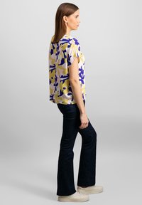 Kortærmet bluse med et blomsterprint i gule, lilla og pink nuancer; afslappet pasform; suppleret med mørk denim flared jeans og hvide sneakers.