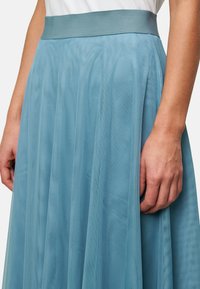 Jupe en tulle bleu clair avec une large ceinture élastique, présentant des plis verticaux et une texture douce et transparente.