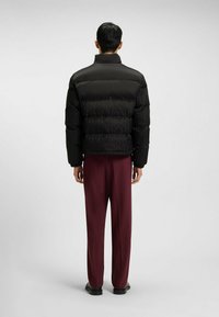 Giacca a vento nera con collo alto e design trapuntato. Abbinata a pantaloni larghi borgogna e scarpe nere.