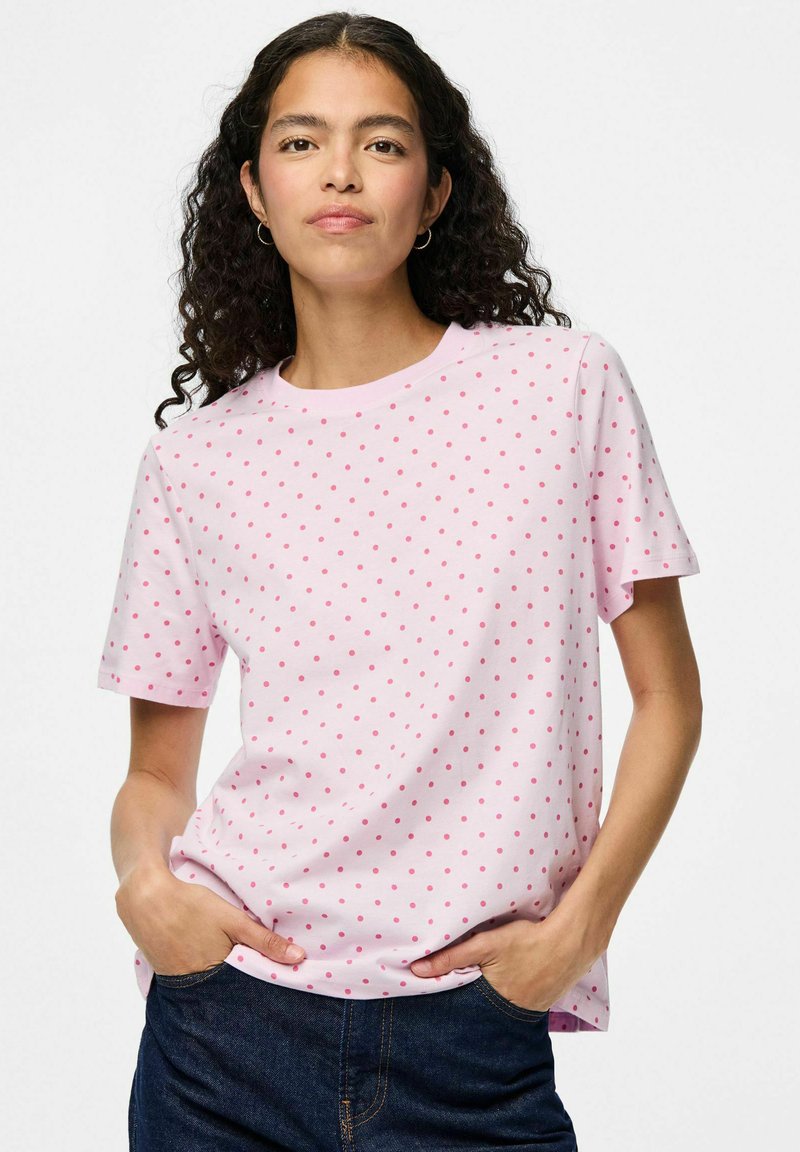 Vaaleanpunainen lyhythihainen t-paita, jossa on valkoinen pilkkukuosi. Paidan materiaali on pehmeä, ja siinä on rento istuvuus sekä pyöreä kaula-aukko.