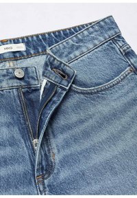 Pantalones vaqueros de denim en azul claro con cierre de cremallera, botón de metal y costuras a contraste. Presentan bolsillos delanteros y una textura desgastada.