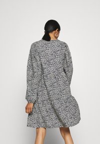 Robe à imprimé floral en bleu marine et blanc, avec des manches longues, une taille cintrée et une jupe évasée. Fabriquée en tissu léger avec une texture douce.
