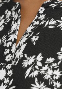 Närbild av svart tyg med vitt blommönster och en v-formad halsringning på medelbrun hud.