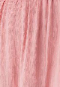 Růžová plisovaná látka se strukturovaným povrchem a vertikálními pruhy, vytvářející měkký, splývavý vzhled. Viditelný detail elastického pasu.